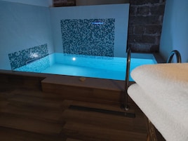 A modern bathroom with a wooden floor, a bathtub with mosaic tiles, and a towel on a wooden bench.
