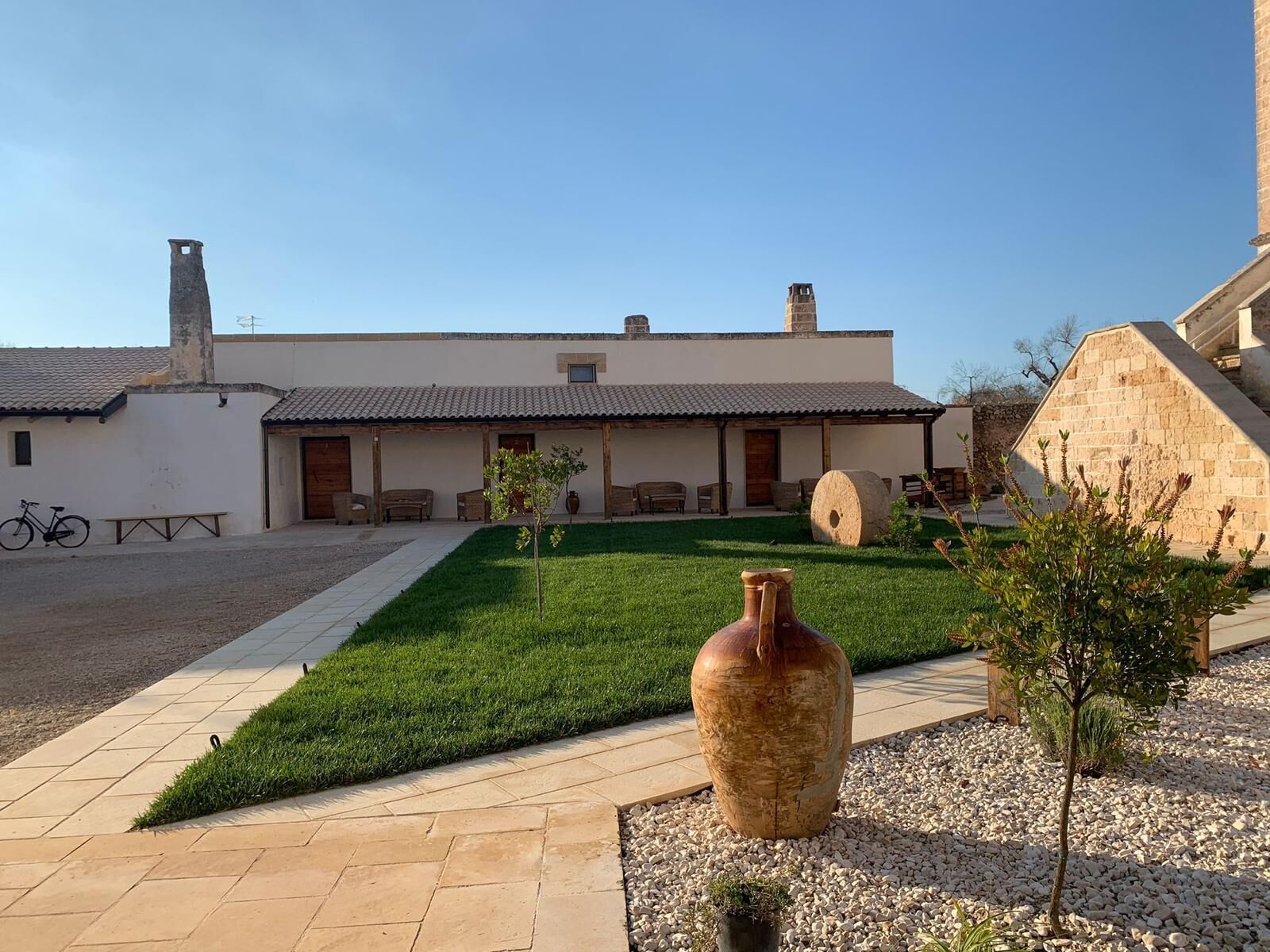 A courtyard with a large vase, a small tree, and a building with a tiled roof.