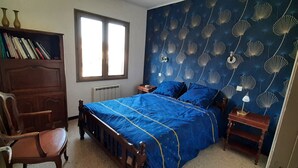 A bedroom with a bed, a wooden wardrobe, a chair, a window, and a wall with a shell pattern.
