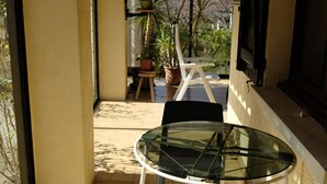 A covered patio with a glass table and chairs, potted plants, and a view of the outside.