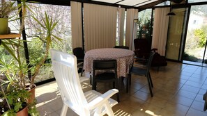 A sunlit patio with a table and chairs, potted plants, and a view of the outdoors.