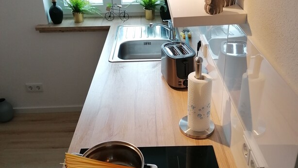 A modern kitchen with a wooden countertop, stainless steel appliances, and a window with a view of trees.