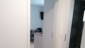 A hallway with a wooden floor, white walls, and a door leading to a bathroom.