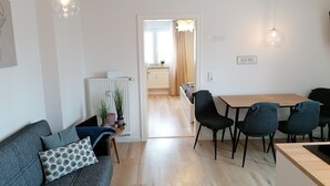 A modern living room with a sofa, a dining table with chairs, and a kitchen area in the background.