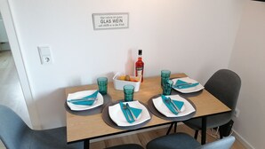 A dining table set with blue napkins, plates, and glasses, a fruit bowl, and a bottle of Aperol.