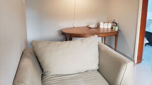A room with a beige armchair, a wooden table with kitchen items, and a hanging light fixture. - Cozy apartment minutes away from downtown, hiking trails, and beach attractions. (Freetown)