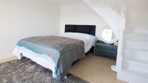 A bedroom with a bed, a dresser, a round mirror, and a staircase. - Beautiful Lofthouse, a cottage on a private beach lot by Lake Mälaren (Ekerö)