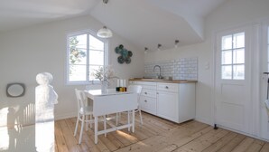 A kitchen with white cabinetry, a wooden floor, and a dining area with white chairs. - Beautiful Lofthouse, a cottage on a private beach lot by Lake Mälaren (Ekerö)