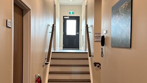 A hotel hallway with a carpeted staircase, a fire extinguisher, a security camera, and a painting on the wall. - The Landing - Extended Stay Quarters (Meaford)