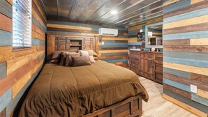 Une chambre à coucher avec une tête de lit en bois, un lit recouvert d’une couverture marron, une commode et un miroir.