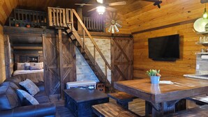L’intérieur d’un chalet rustique comprend une chambre à coucher située en mezzanine, un escalier en bois et un coin repas avec des bancs.