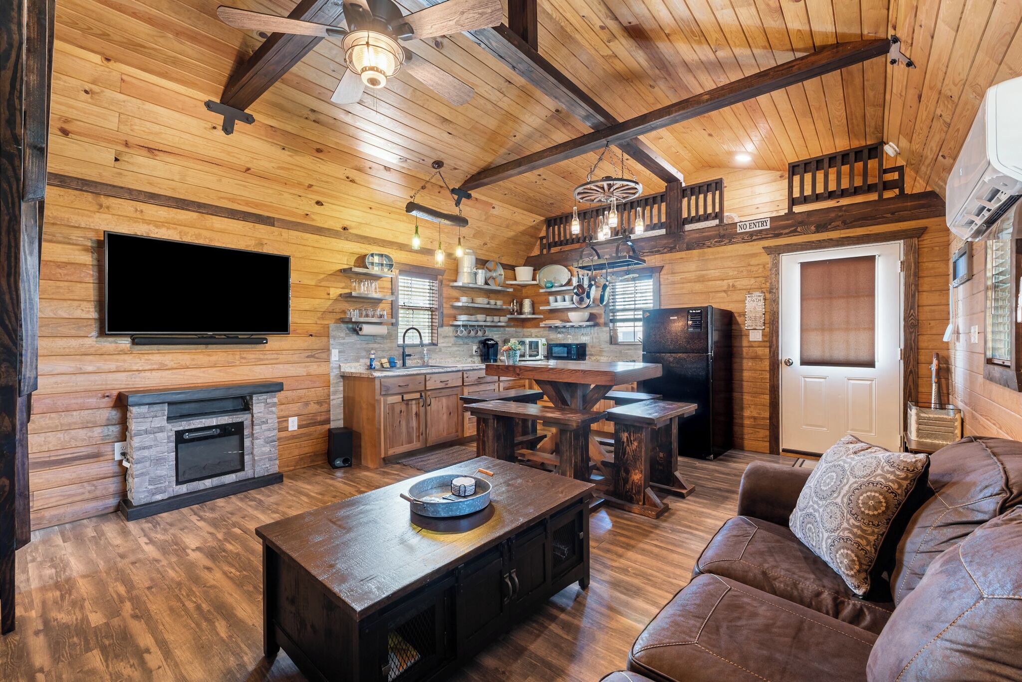 A cozy cabin interior with a wooden interior, a fireplace, a dining area, and a living room with a sofa.