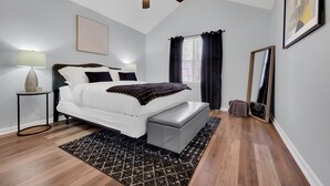 Un dormitorio con cama, mesitas de noche, ventilador de techo, ventana con cortinas y un espejo.
