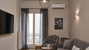 A modern living room with a grey sofa, a patterned armchair, a small round table, and a flat-screen TV mounted on the wall. - Ilisia Park Contemporary 2BD Condo (Athens)