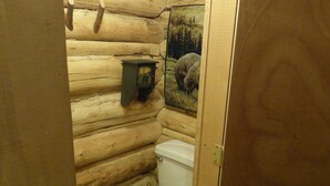 Une petite salle de bain de style cabane en bois, avec des toilettes, un banc en bois et un tableau encadré au mur.