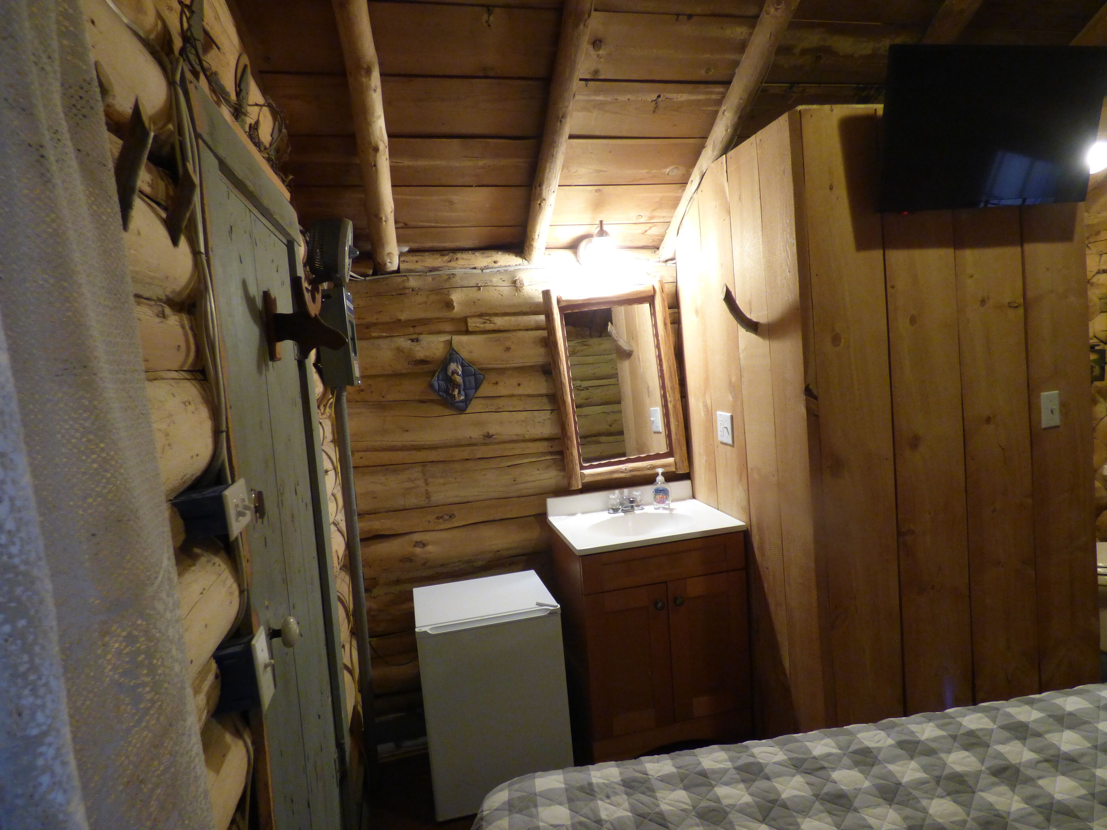 A wooden cabin room with a bed, a small sink, and a mirror.
