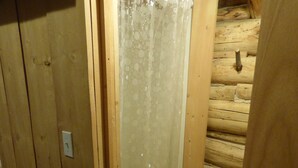 Une cabane en bois avec un espace douche, un interrupteur visible et une porte.