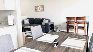 Ein modernes Wohnzimmer mit einer Couch, zwei Sesseln, einem Couchtisch und einem Esstisch mit Untersetzern.