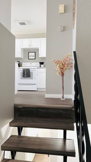 Un escalier menant à une cuisine avec des meubles blancs et un tableau encadré accroché au mur.