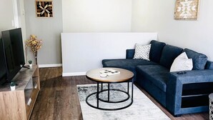 Ein modernes Wohnzimmer mit einem dunkelblauen Sofa, einem runden Couchtisch, einem Flachbildfernseher und Wandkunst.