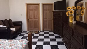 Una habitación con piso a cuadros, un sofá, un aparador, un televisor y dos puertas.