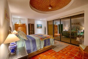 Un dormitorio con cama, mesita de noche, lámpara, cómoda y puerta corrediza de vidrio que da a un balcón.