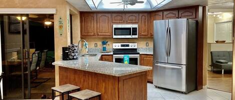 A kitchen with wooden cabinets, a stainless steel refrigerator, a microwave, and a central island with stools.