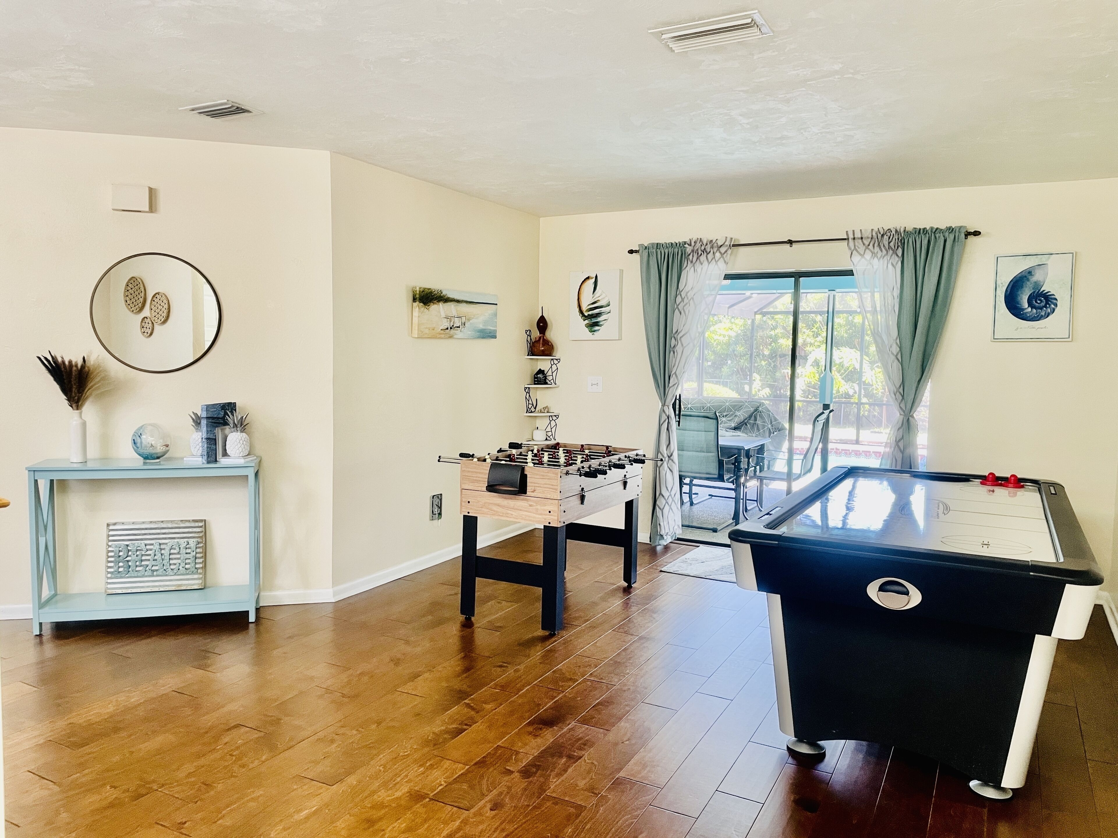 A spacious living room with a wooden floor, a foosball table, a pool table, and a dining area with a table and chairs.