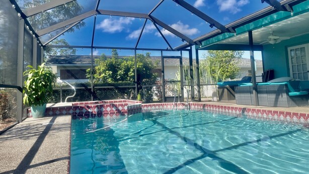 A covered swimming pool with a glass enclosure, surrounded by a patio area with seating and a potted plant.