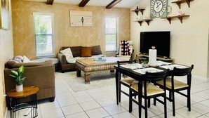 A living room with a sofa, coffee table, TV, and a dining area with chairs and a table.