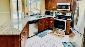 A modern kitchen with granite countertops, wooden cabinets, stainless steel appliances, and a large window providing natural light.