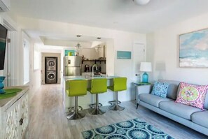 Eine moderne Küche mit einer zentralen Kochinsel, grünen Barhocker, einem grauen Sofa und einem gemusterten Teppich.