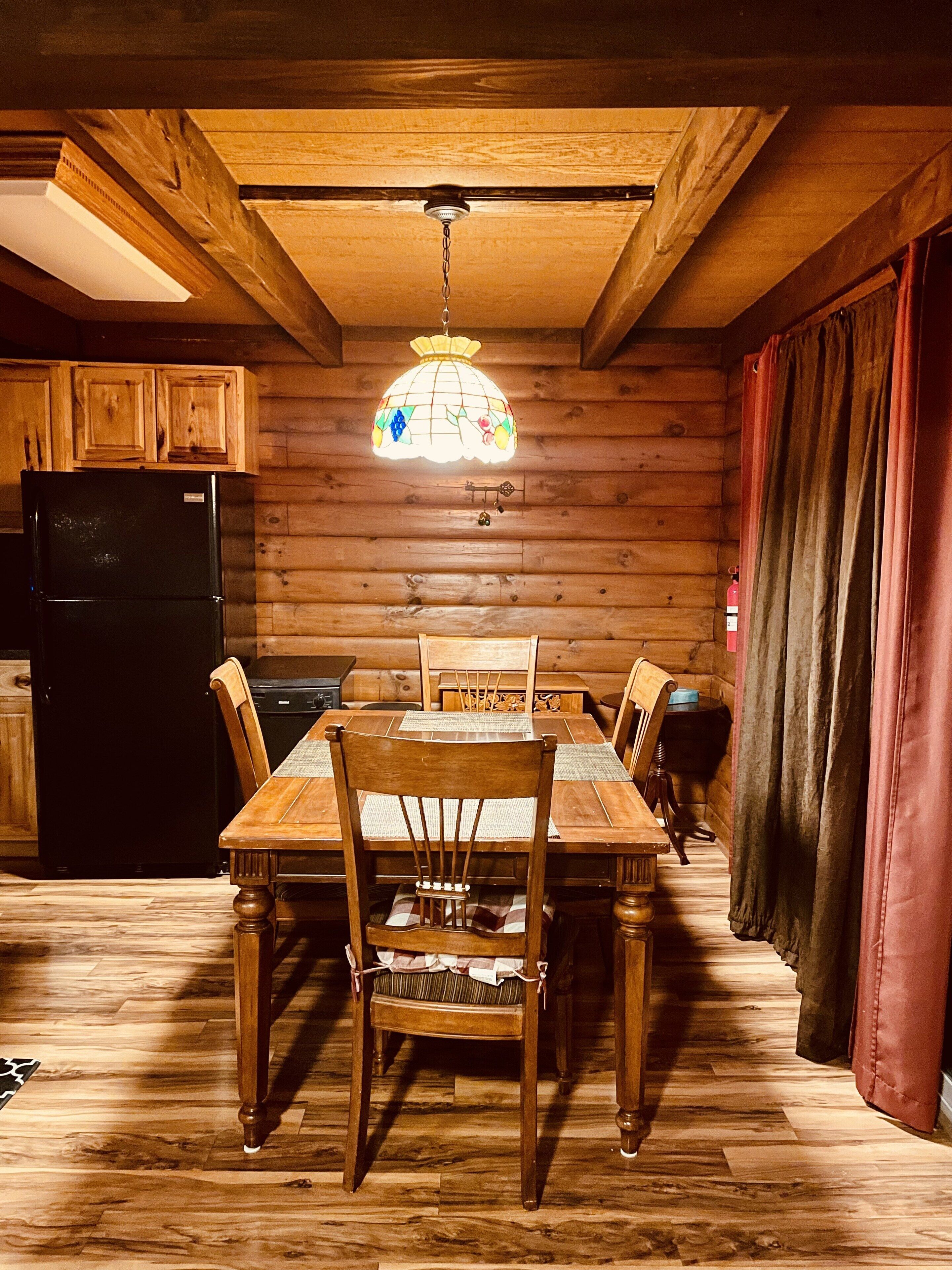 Un interno in legno con un tavolo da pranzo, sedie, un frigorifero e una lampada a sospensione.