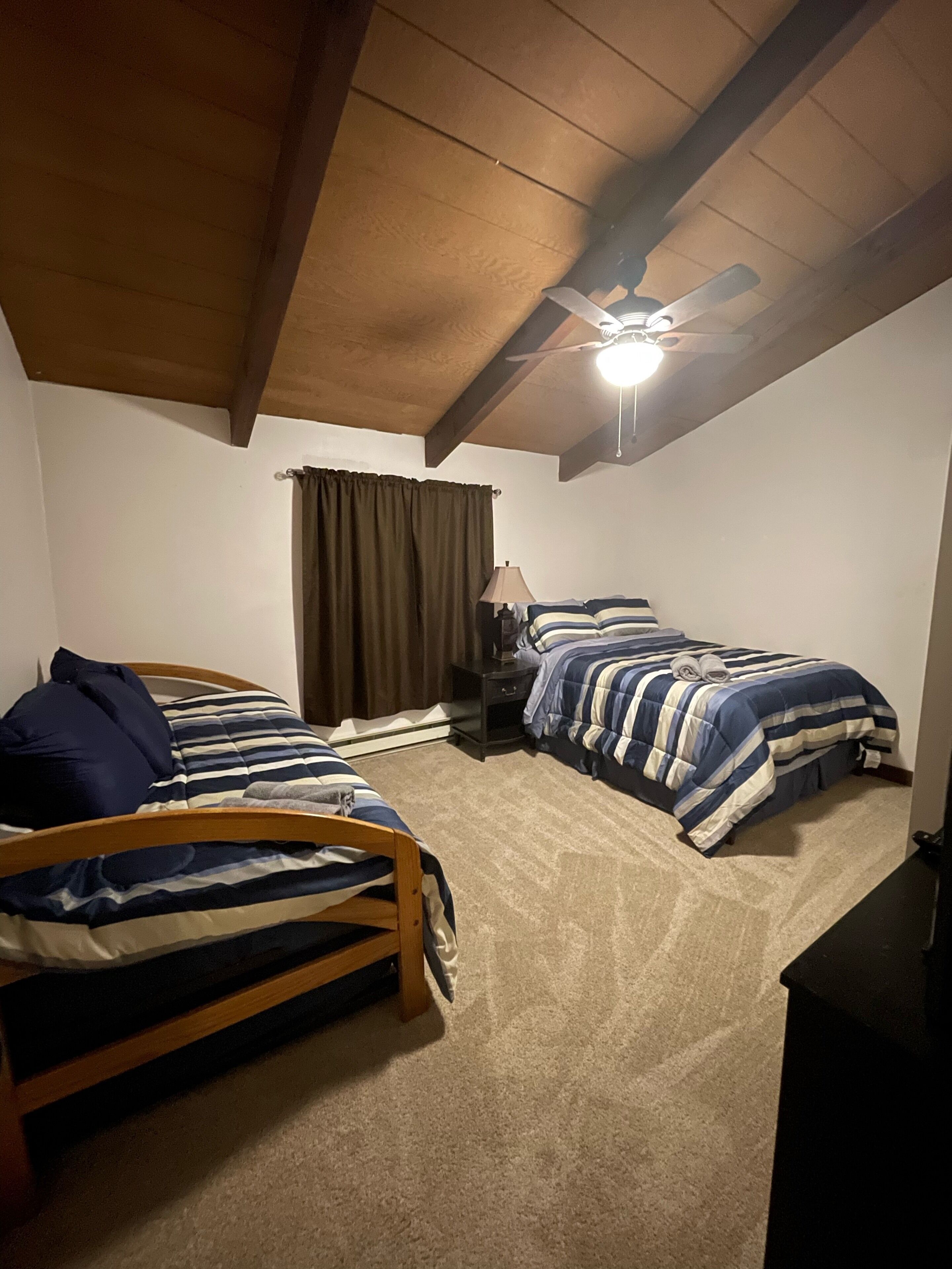 A bedroom with two beds, a ceiling fan, a nightstand, and a window with curtains.