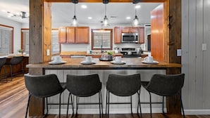 Una cocina moderna con armarios de madera, una isla central con taburetes y luminarias colgantes.
