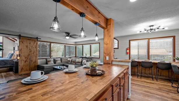 Una cocina amplia con una isla de madera, taburetes de bar y ventanas grandes.