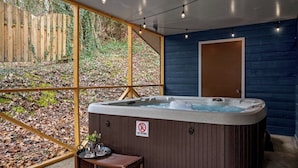Un jacuzzi con un cartel de "No Diving", una mesa de madera con vasos y vistas a un jardín cubierto de hojas a través de grandes ventanales.