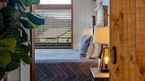 Un dormitorio con cama, mesita de noche, lámpara y un ventanal grande.