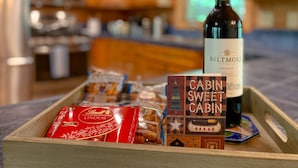 Un vassoio di legno con una bottiglia di vino della tenuta Biltmore, una scatola con la scritta 'Cabin Sweet Cabin' e diverse confezioni di cioccolatini Lindor.