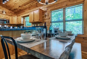 A wooden cabin kitchen with a large island, wooden cabinets, and a view of greenery through the windows.