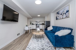 A modern living room with a blue sofa, a coffee table, and a flat-screen TV mounted on the wall.
