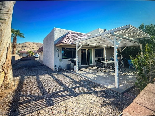 Una casa con patio, un área de estar techada al aire libre y una montaña al fondo.