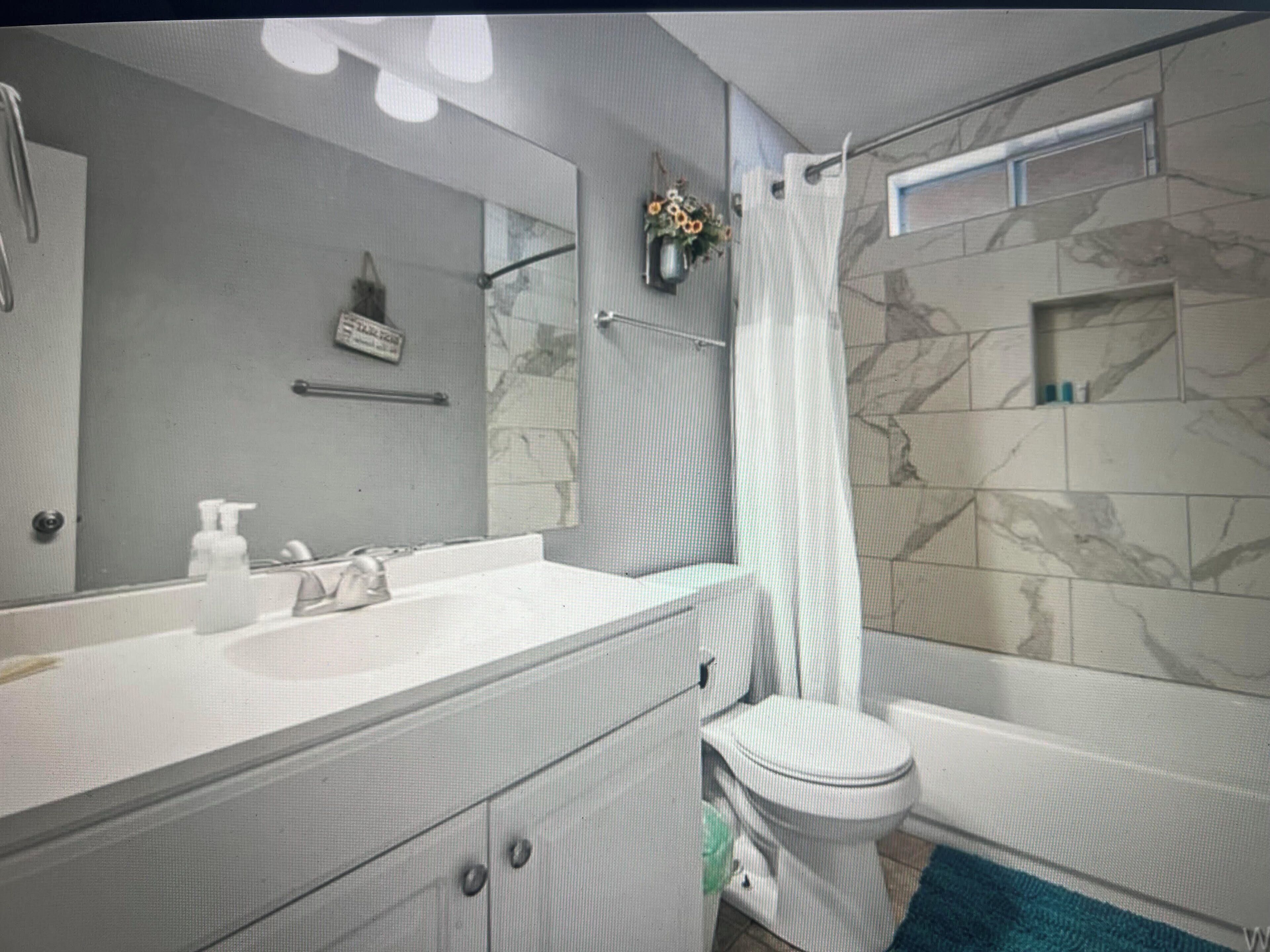 Un baño con lavamanos blanco, espejo, inodoro y cortina de ducha.