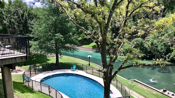 Une piscine à bord incurvé, entourée d’une clôture métallique et d’une zone herbeuse.