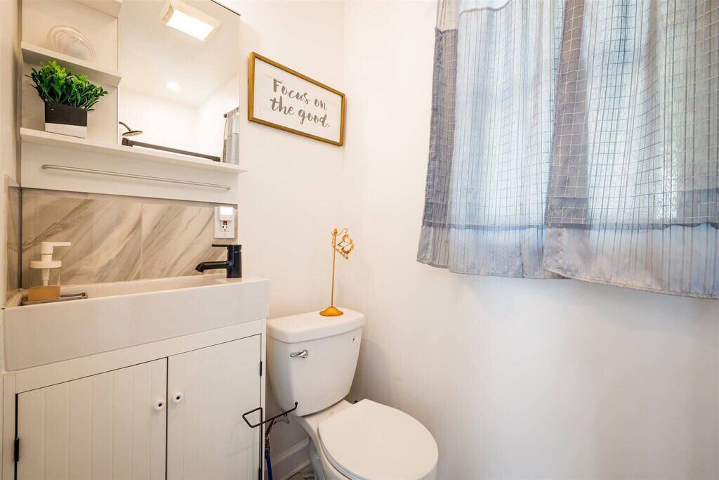 Une salle de bain moderne équipée de toilettes, d’un lavabo, d’un miroir et d’une étagère sur laquelle est posée une plante.