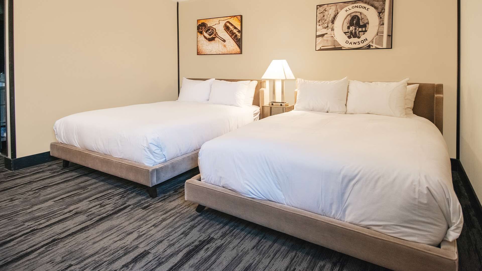 Habitación de hotel con dos camas, una lámpara y dos cuadros en la pared.