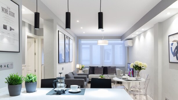 Een moderne keuken met een centraal eiland, hanglampen en een eethoek met transparante stoelen.