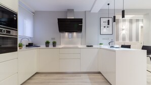 Een moderne keuken met witte kastjes, een Bosch oven, een roestvrijstalen afzuigkap en een klein keukeneiland met een spoelbak en aanrecht.