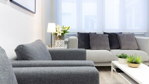 Een moderne woonkamer met grijze banken, een witte salontafel en een raam met zonwering.
