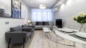 Een moderne woonkamer met een bank, een bijzettafeltje en een eethoek met een glazen tafel en stoelen.